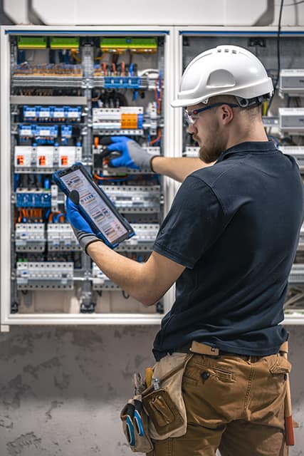 electrical technician working in a switchboard with fuses, uses a tablet. electrical technician working in a switchboard with fuses, uses a tablet.
